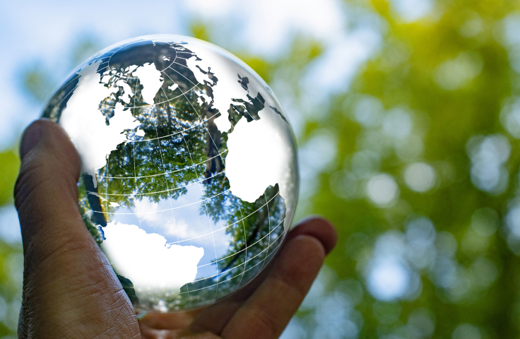 Focus on taking care of nature and the climate shown with a globe around a crystal ball with nature reflected inside and outside the ball. The ball is held by one hand