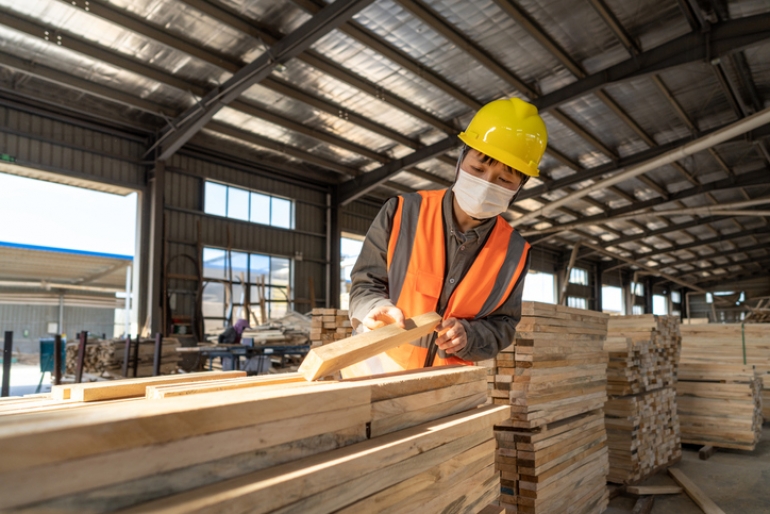 A Chinese worker wearing a mask inspects wood in a warehouse