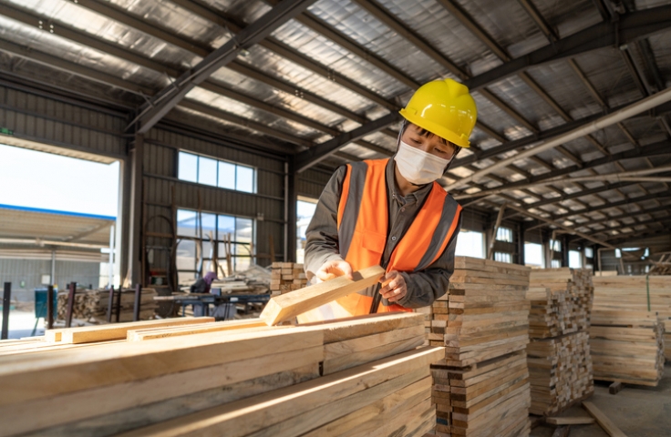 A Chinese worker wearing a mask inspects wood in a warehouse